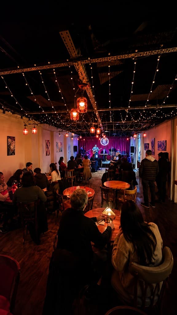 Interior de La Llama: sala con luces, mesas, público y banda en vivo en el escenario con cortina roja y neón.